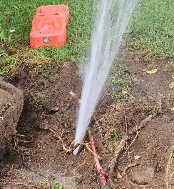 Burst water main spraying from a trench during an emergency repair